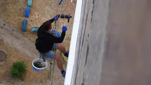 Alpinista industrial suspenso em cordas isola fachada com isopor perto da parede
