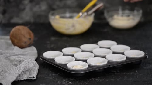 Filling the paper molds with dough to make muffins.