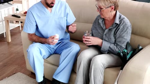 Caregiver Giving Pill to Senior Woman at Home