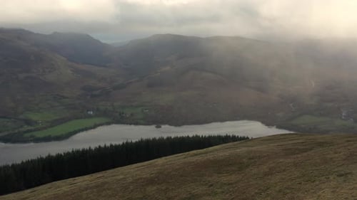 Aerial View of a Riverbank in Surrounded By Hills and Trees on a Foggy Day