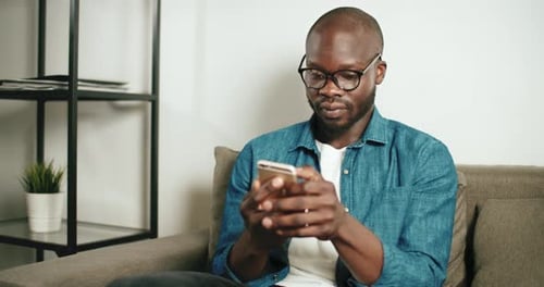 Man Using Smartphone Sitting on Couch Indoors