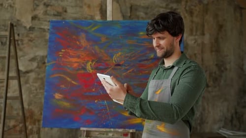 Male Artist is Standing in His Studio and Using a Tablet Working on a Project