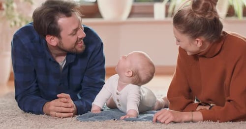 Smiling Young Couple Lying Together on Rug on Their Living Room Floor at Home with Their Adorable