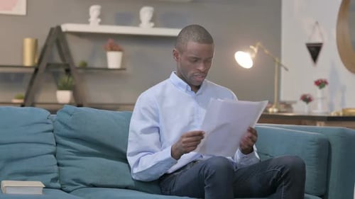 Young Adult Reading Documents at Home on Sofa
