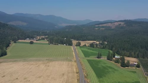 Aerial of cars traveling on a rural farm road with beautiful scenery around it.