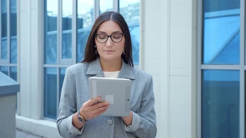 Woman in a Formal Suit and Glasses Looks Into a Tablet on the Street Slow Motion