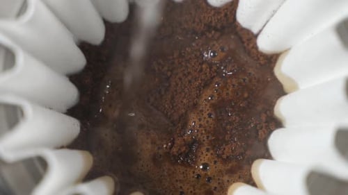 Hot water pour over into ground coffee beans close up slow motion