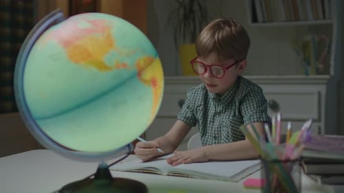 Preschool Boy Studying Earth Globe on the Table with School Books