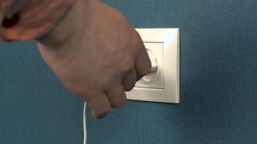 A Man Pulls Out a Phone Charger From a Wall Outlet. Rosette in the Wall with Dark Blue Wallpaper