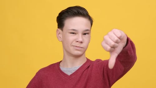 Teenager Boy Gesturing ThumbsDown Shaking Head In Disagreement Yellow Background