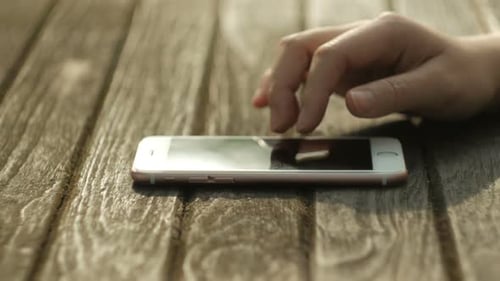 Hand Interacting with Smartphone on Wooden Table