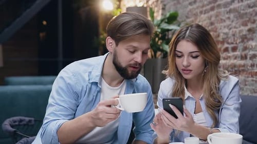 Guy and Blond Woman with which Sitting Together in Hotel and Drinking Tea During Using Phone