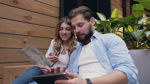 Moderne junge Frau und Mann, die auf einer weichen Couch in der Hotelhalle sitzen und Tablet PC und Karte benutzen