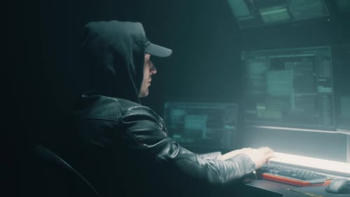 Hooded Coder Working at Illuminated Multi-Monitor Desk