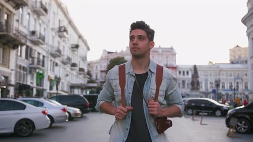 Attractive Young Handsome Man Tourist with Backpack Walking in City Center and Looking Around Slow