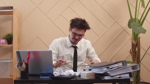 Office Worker with Tousled Hair and an Irritated Look Writes Something on Paper and Abruptly Throws