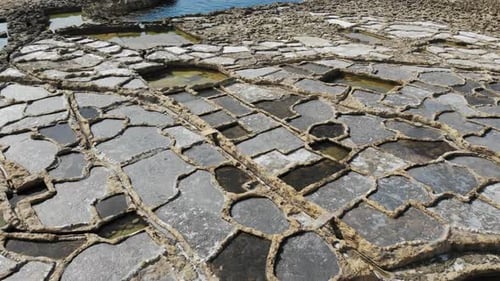 A slow, low-level aerial drone shot skims across the Salt Pans of Gozo island in Malta.