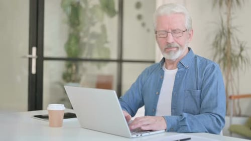 Senior Man Types at Laptop in Home Office