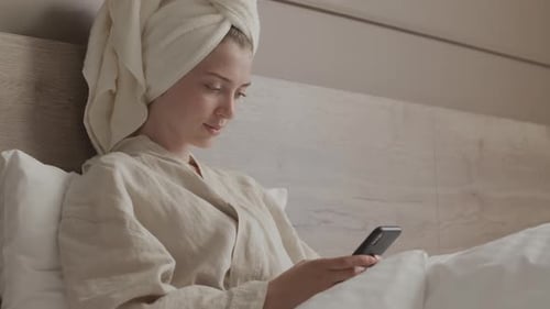 Woman Relaxing in Bed with Smartphone and Towel