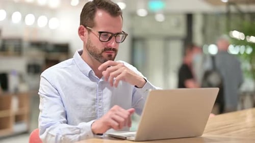 Pensive Businessman Thinking and Working on Laptop in Office
