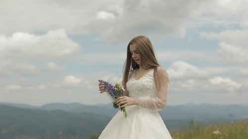 Woman in Dress Holding Flowers in Mountain Field