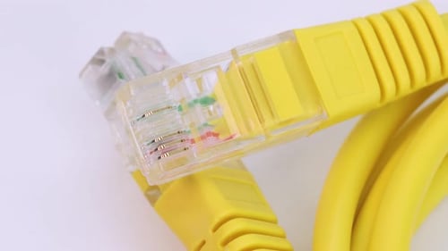 Macro shot of ethernet cable of yellow plastic rotating on white surface, close up view from above i