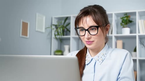 Happy young woman freelancer in glasses works for a laptop.