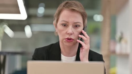 Close Up of Old Businesswoman with Laptop Talking on Smartphone