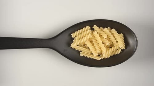 Adding Dried Pasta To A Black Spoon