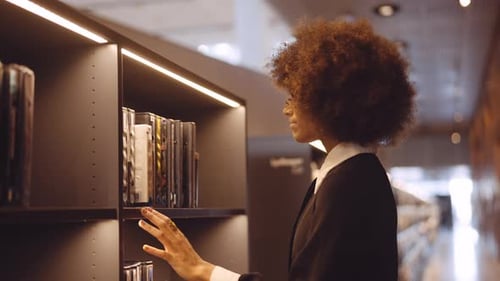 Young Woman Choosing Book From Library Shelf