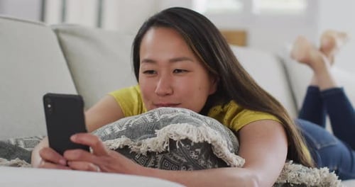 Woman Relaxes On Couch With Her Smartphone