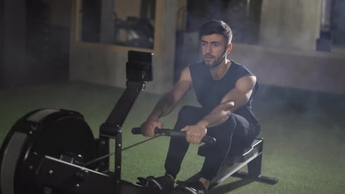Handsome Athlete Works Out in Gym with Rowing Machine