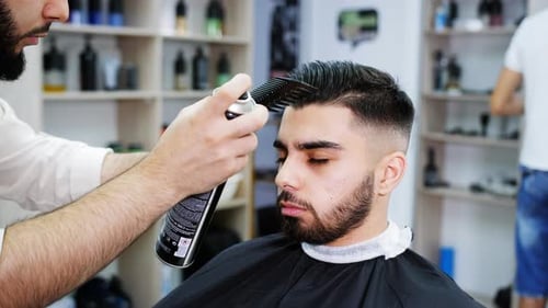 Barber Styles Young Man's Hair With Hairspray and Comb