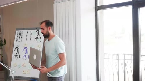 Creative Man Working on His Laptop Next to the Window and Moving at His Desk Office