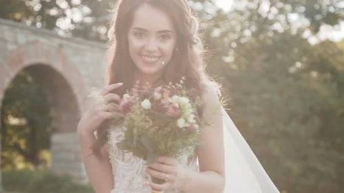 Happy Bride with Bouquet in Hands Smiles and Poses at Ancient Castle