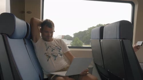 Ansicht eines jungen Mannes, der während der Reise im Zug sitzt und Laptop gegen das Fenster benutzt, Niederlande