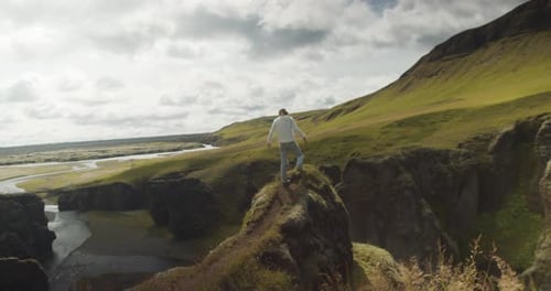 Back view of young hiker with raised hands on the edge of a cliff