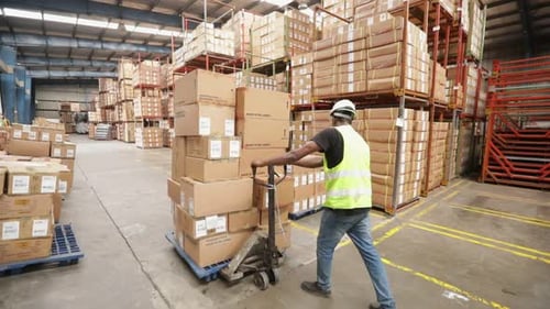 Warehouse Worker Pushes A Hand Pallet Truck With Boxes