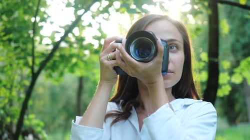 Pretty Smiling and Laughing Girl Photographer Wearing White Shirt Is Making Photos in a Park