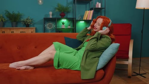 Happy Relaxed Girl in Wireless Headphones Dancing Listening Favorite Rock n Roll Music on Home Couch