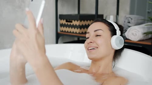 Красивый Брюнет слушает музыку через наушники и использует смартфон, принимая ванну в квартире , Стоковые видеоматериалы Включая: зависимость и квартира - Envato