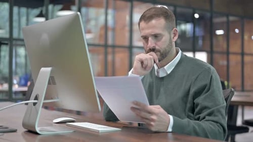 Ambitious Man Reading Document on Office Desk