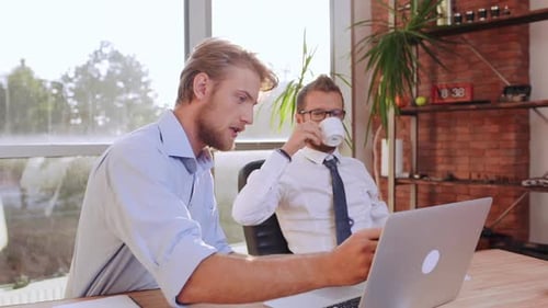 Young Men Work at Desk, One Naps