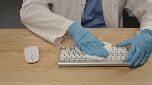 Healthcare Professional Disinfecting Keyboard and Mouse at Desk