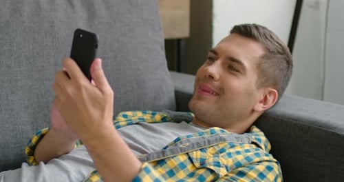 Young Man in Casual Clothes, Lying on Sofa, Using His Smartphone, Close Up