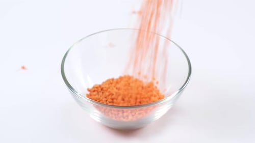 Red Lentils Pouring Into Glass Bowl