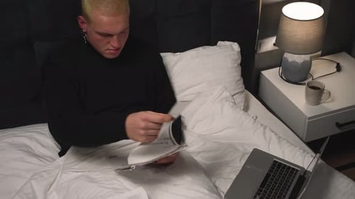 Man Reviews Documents in Bed with Laptop