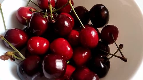 Gros plan d'un bouquet de cerises sur un bol en céramique blanche. Certains ont encore leur queue. Ils sont mûrs