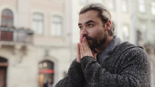 Man Warming Hands Outdoors in Urban Setting