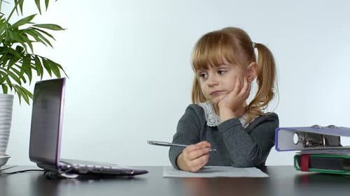 Young Girl Writes at Desk with Laptop